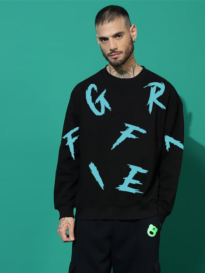 Man wearing a black sweater with blue text and black pants on a teal background