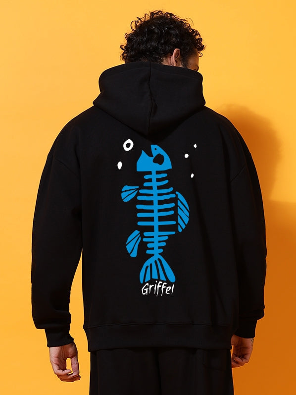 Person wearing a black hoodie with a blue fish skeleton design on an orange background
