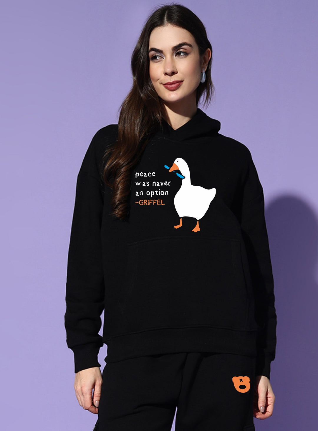 Person wearing a black hoodie with a graphic and text, standing against a purple background