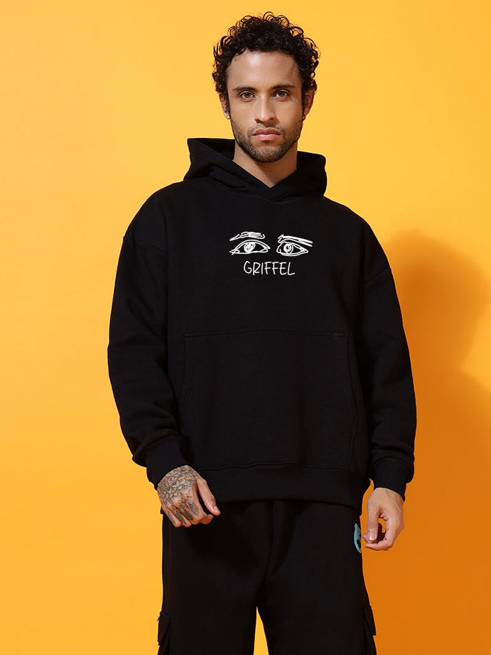 Person wearing a black hoodie and pants with a brand logo on an orange background
