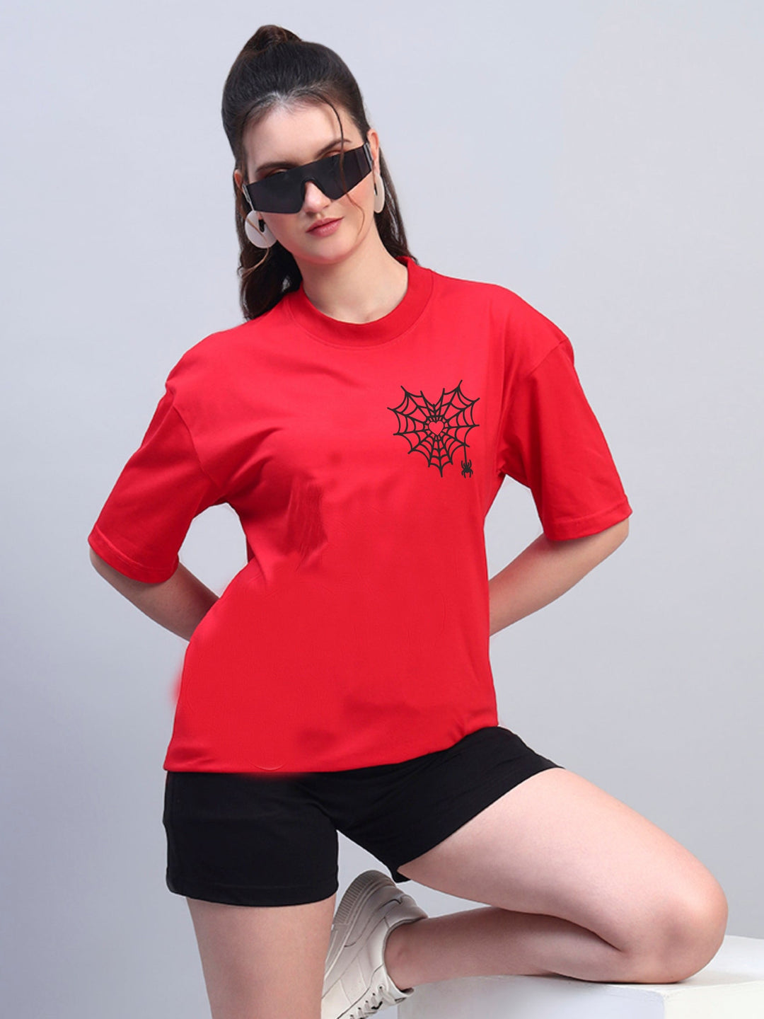 Person wearing a red t-shirt with a black design, black shorts, and white sneakers on a light gray background.