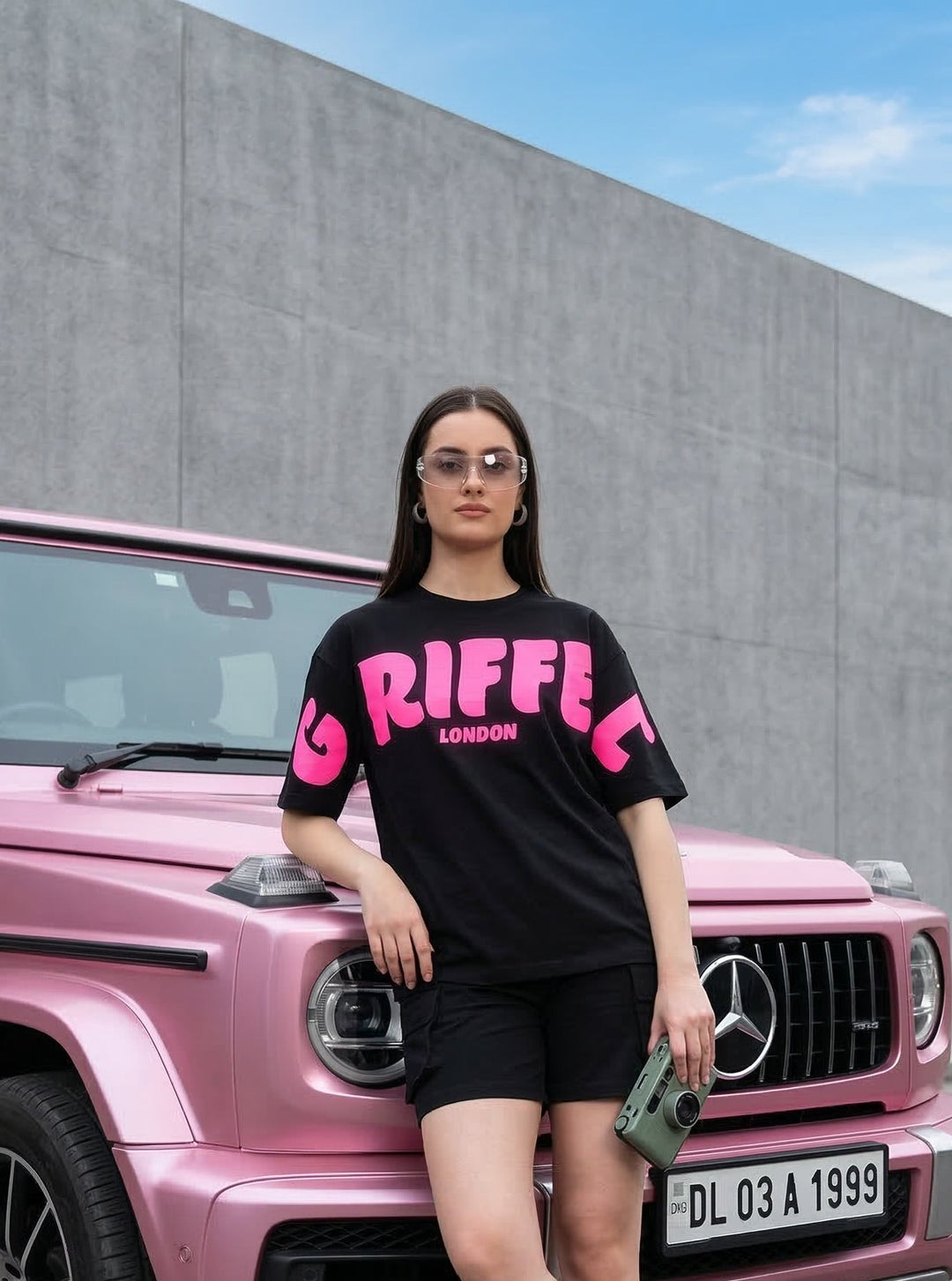 Woman in a black t-shirt with pink text standing next to a pink Mercedes-Benz G-Class.